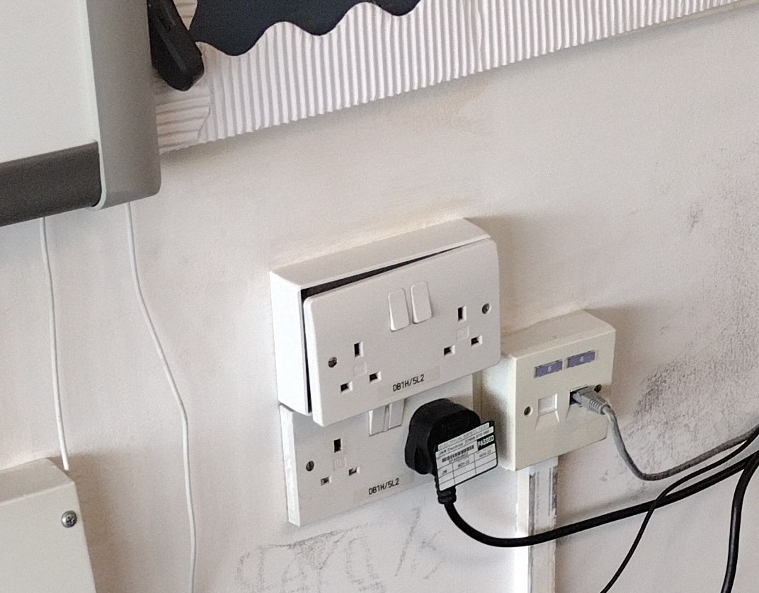 wall-mounted plastic socket outlet with loose faceplate exposing interior of box
